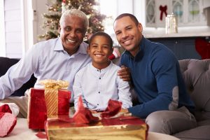 Grandson With Grandfather And Father Opening Christmas Gifts