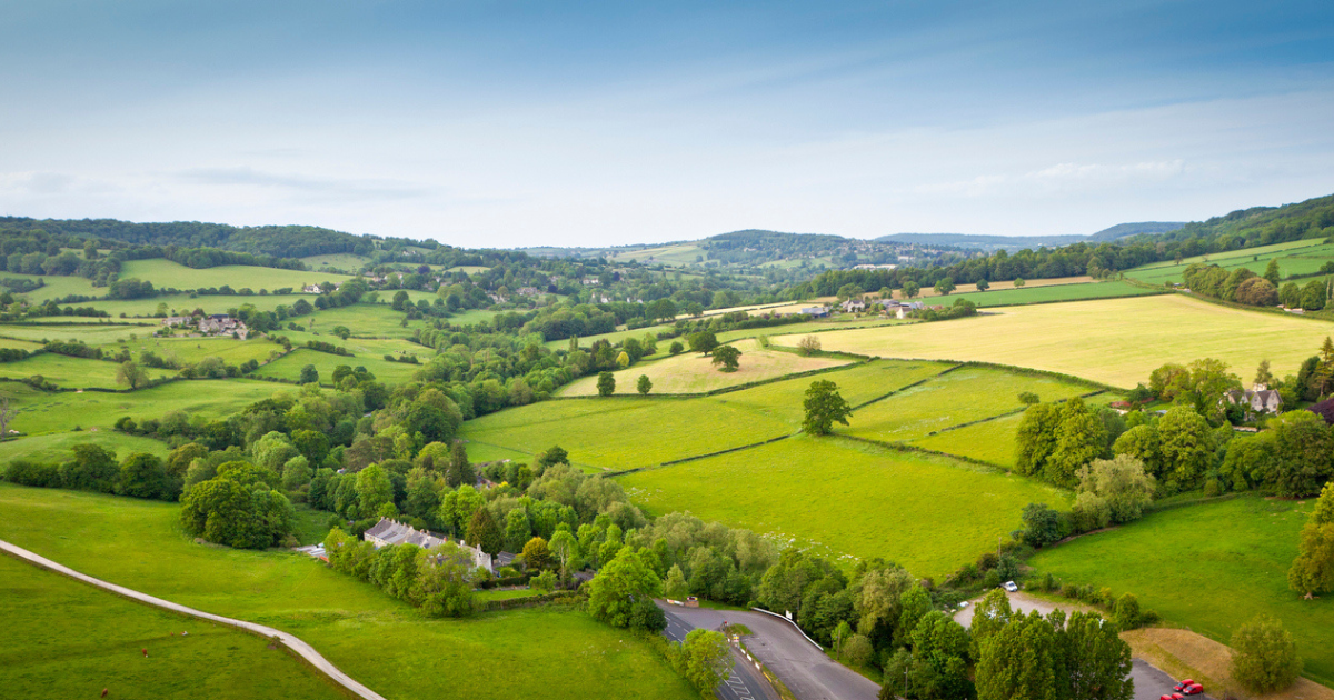 Dramatic aerial view of gently rolling patchwork farmland with pretty wooded boundaries, in the beautiful surroundings of the Cotswolds