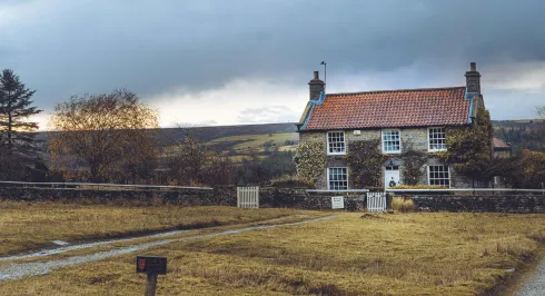 Traditional stone cottage with orange tile roof under dramatic cloudy sky in rural countryside setting