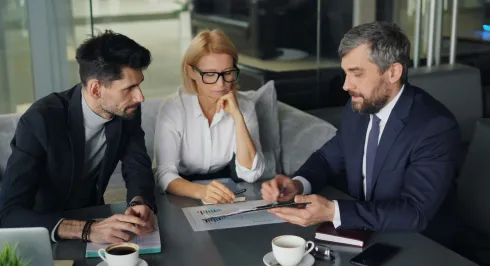 Professionals reviewing financial documents during office meeting with coffee